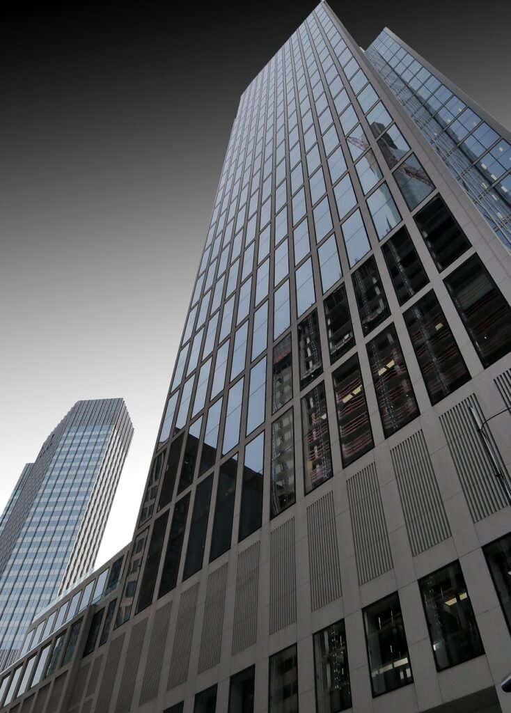Modern glass office skyscraper viewed from a low angle, featuring reflective windows and clean architectural lines.