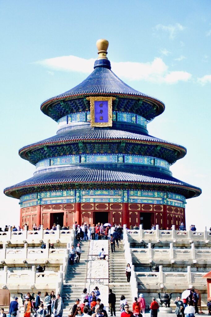 Visitors walking up stone steps toward the Temple of Heaven, a circular blue-roofed imperial temple in Beijing, China.