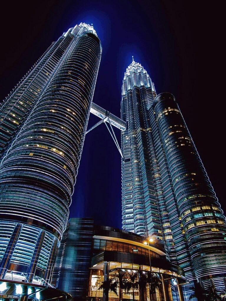 Petronas Twin Towers illuminated at night in Kuala Lumpur, viewed from below with the skybridge connecting the two skyscrapers.