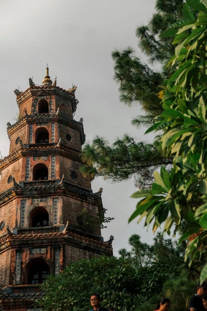 Destination Historic multi-tiered brick pagoda tower surrounded by green trees under a cloudy sky.