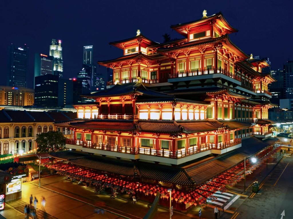Illuminated multi-tiered Chinese temple at night with red lanterns, set against a modern city skyline.