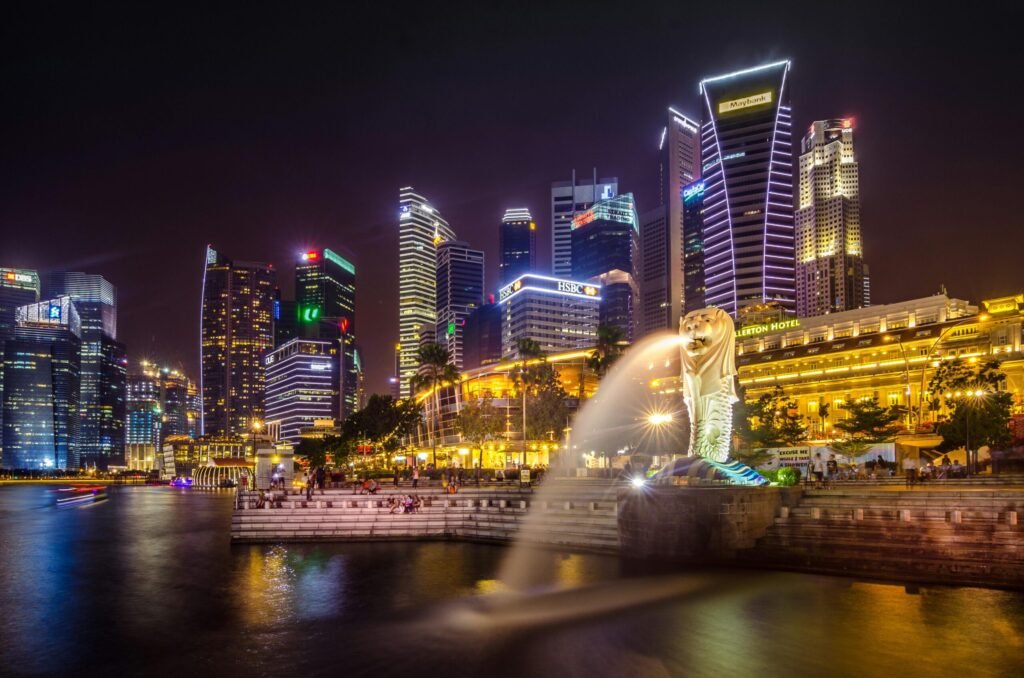 Night view of Singapore’s illuminated skyline with the Merlion statue spouting water into Marina Bay.