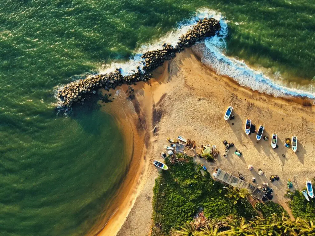 Destination Aerial view of a srilanka beach with small fishing boats, green water, and a rocky breakwater.
