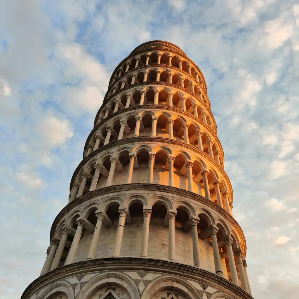 Destination Upward view of the Leaning Tower of Pisa against a partly cloudy sky.