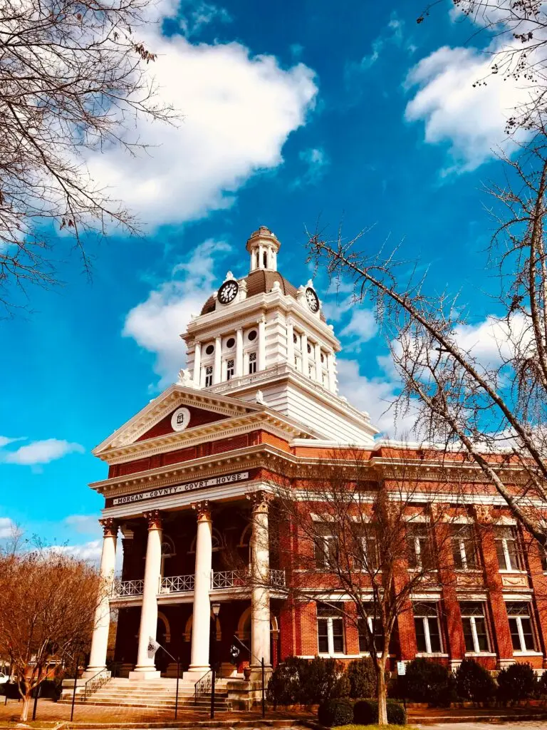 Historic Morgan County Courthouse with a clock tower, red brick façade, and white columns under a blue sky.