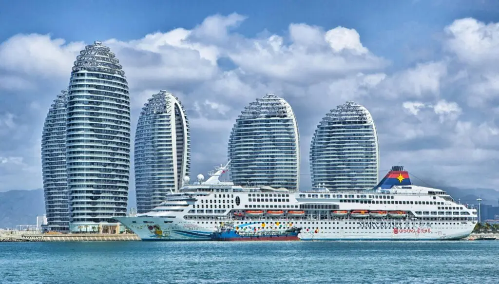Destination Large cruise ship sailing in front of modern curved high-rise buildings along a coastal waterfront.
